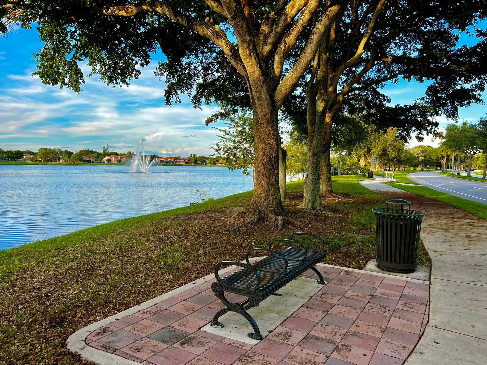 Winston Park Lake in Coconut Creek, FL, with a fountain, a live oak and a bench at sunset